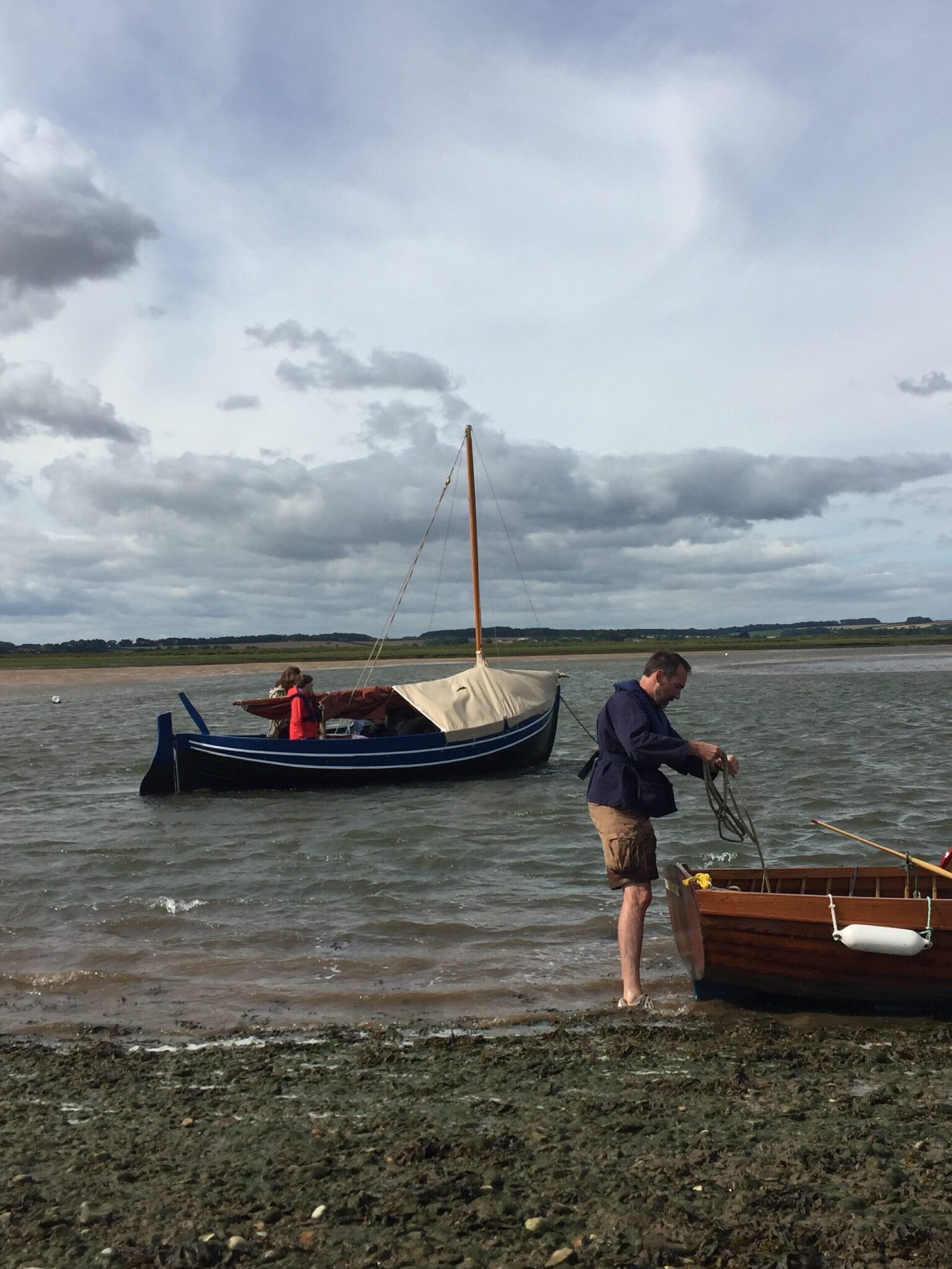 Man on a shore ties a rope to a small wooden boat