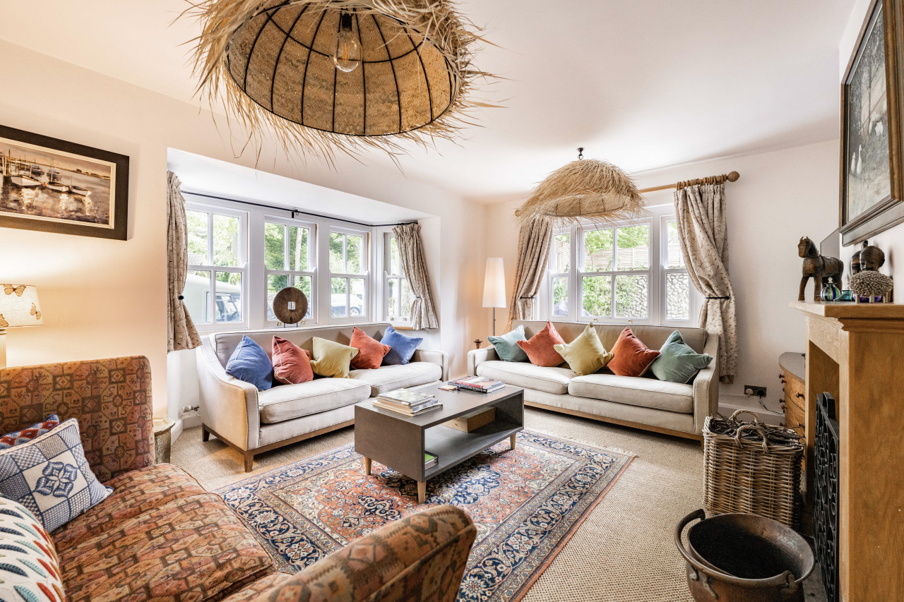 cozy living room with two large white sofas adorned with colorful pillows. A patterned rug and woven lampshade add warmth. Bright, inviting ambiance