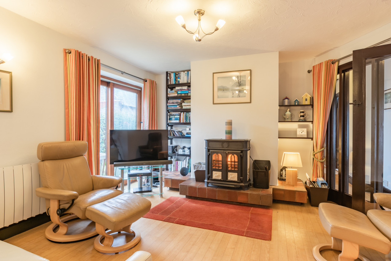 Cozy living room with a leather recliner, TV on a stand, wood-burning stove, and bookshelves. Warm tones and soft lighting create a welcoming atmosphere.