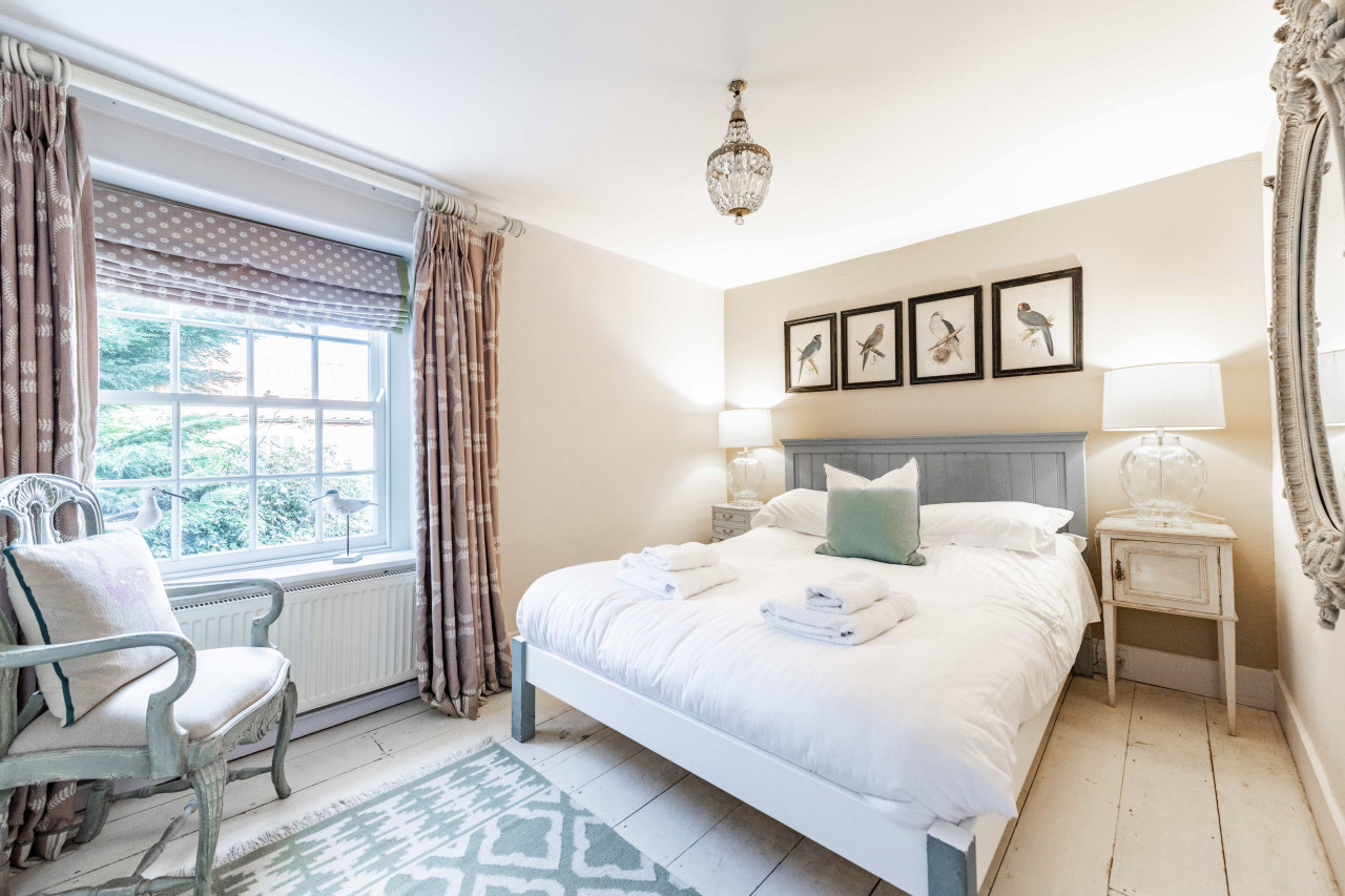Cozy bedroom with a plush, white bed adorned with towels and a green cushion, flanked by vintage nightstands. Bird artwork hangs above, creating a serene atmosphere.