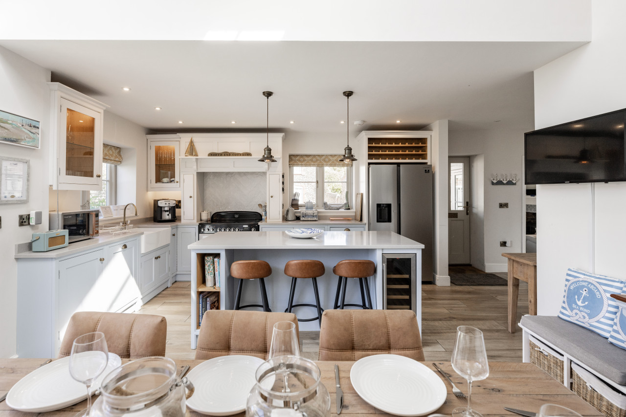 Spacious, modern kitchen with an island, brown bar stools, and stainless steel appliances. Bright and airy with a cozy dining area in the foreground.